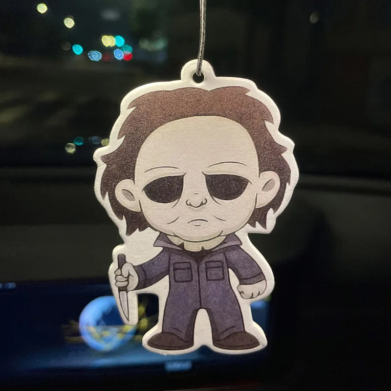 Cartoon character air freshener with dark hair and sunglasses, hanging against a blurred background.