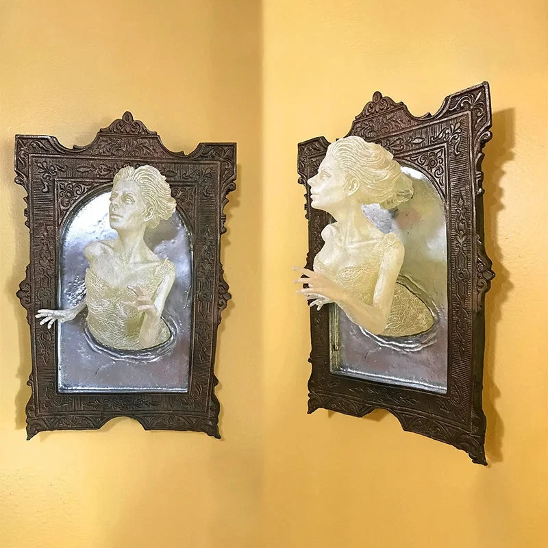 Two decorative wall art pieces with classical busts in ornate frames on a yellow wall.