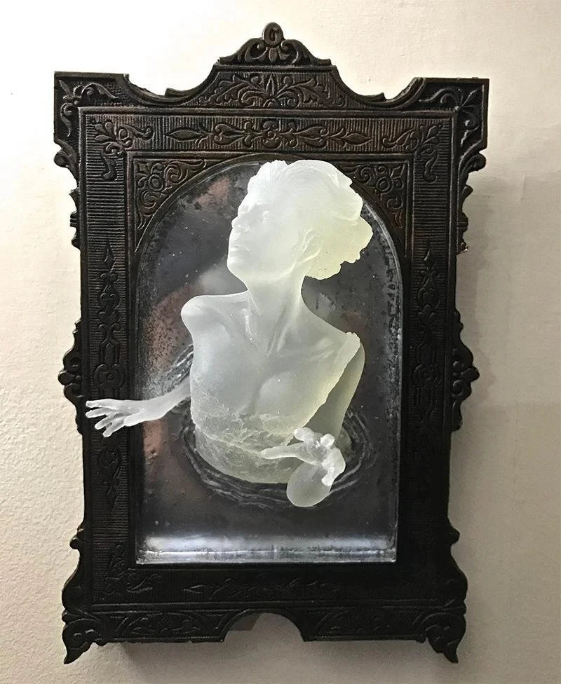 Decorative wall art with a black frame and a white sculpture of a woman's torso.