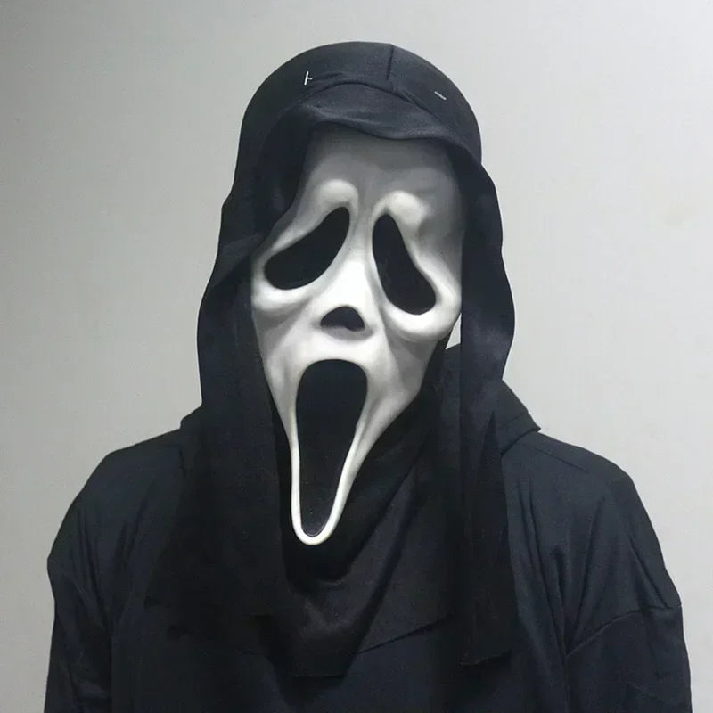 Person wearing a black hooded garment and a white mask with a black mouth and eyes against a plain background