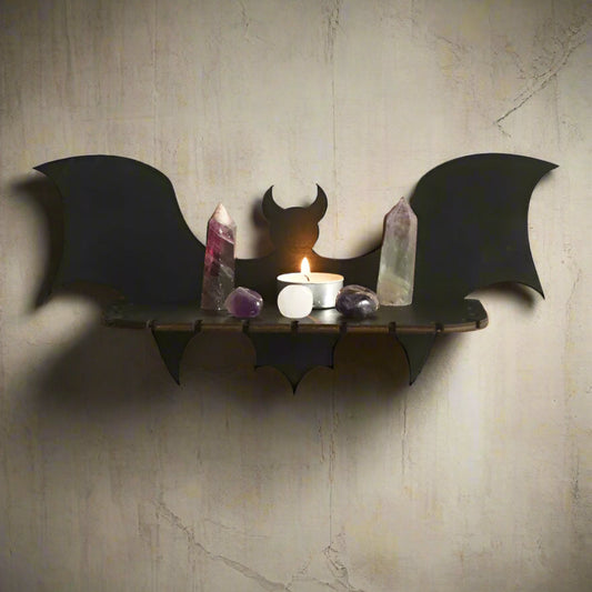 Bat-shaped wall shelf with a candle and crystals on a white wall.
