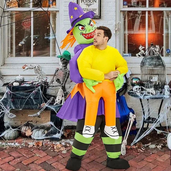 Person in a Halloween costume with a large inflatable witch figure in front of a decorated house.