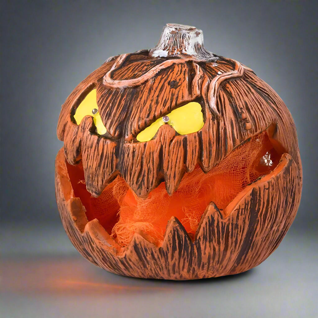 Halloween pumpkin with carved face on a white background with black tree branches and graves.