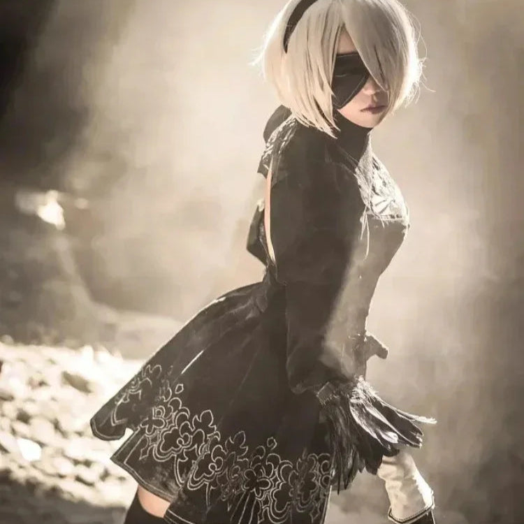 Person in a black outfit with white hair and a blindfold standing in a misty, rocky landscape.