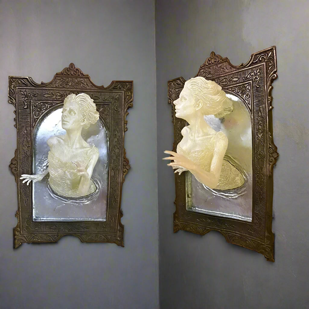 Two wall-mounted sculptures of women in ornate frames on a yellow wall.
