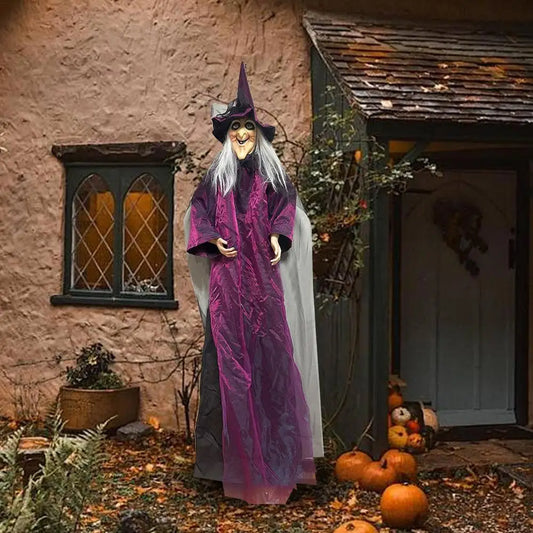 Halloween decoration of a witch in a purple dress with pumpkins and a rustic house in the background.
