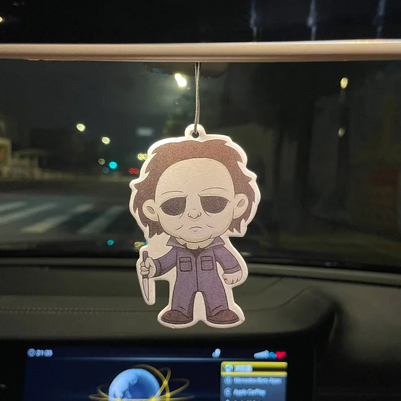 Cartoon character air freshener hanging from a car's rearview mirror at night.