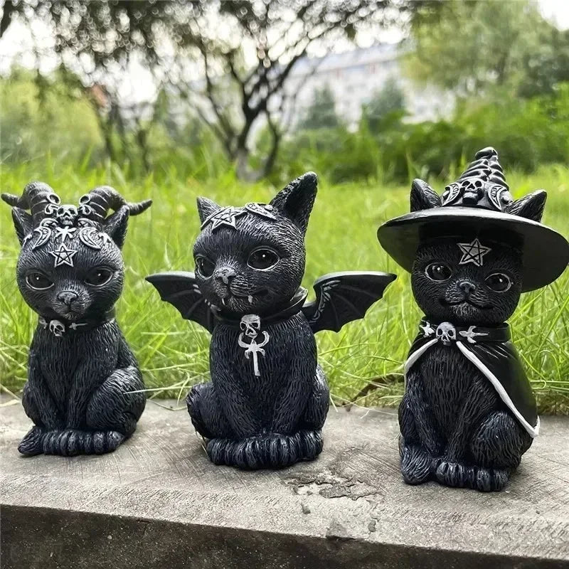 Three black cat figurines with different accessories on a stone surface with a grassy background.