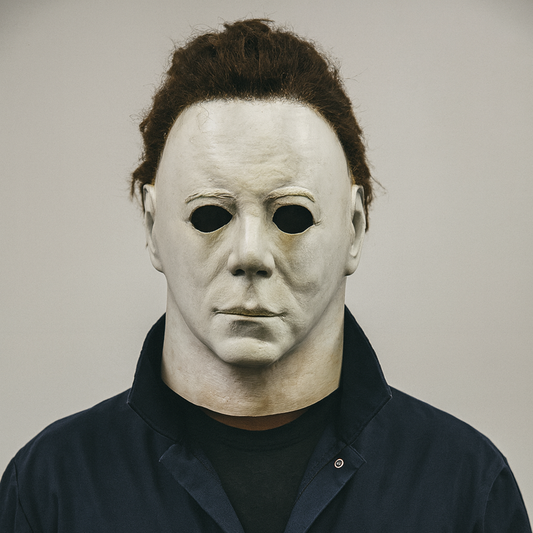 Person wearing a white mask with black eyes and a dark blue jacket on a plain background