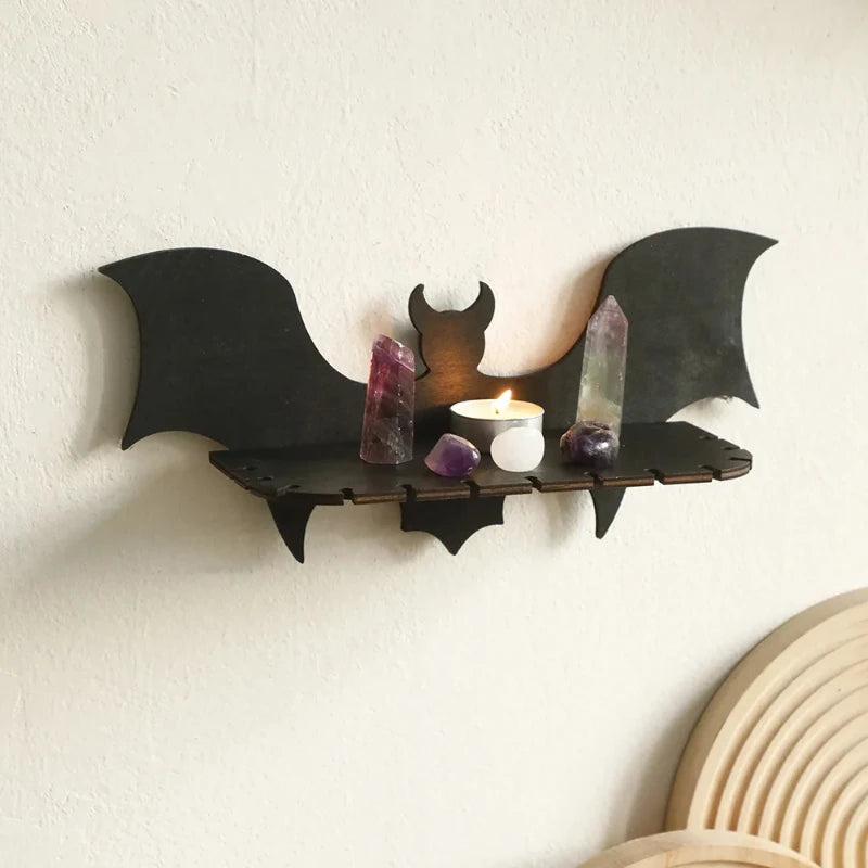 Bat-shaped wall shelf with crystals and a candle on a white wall