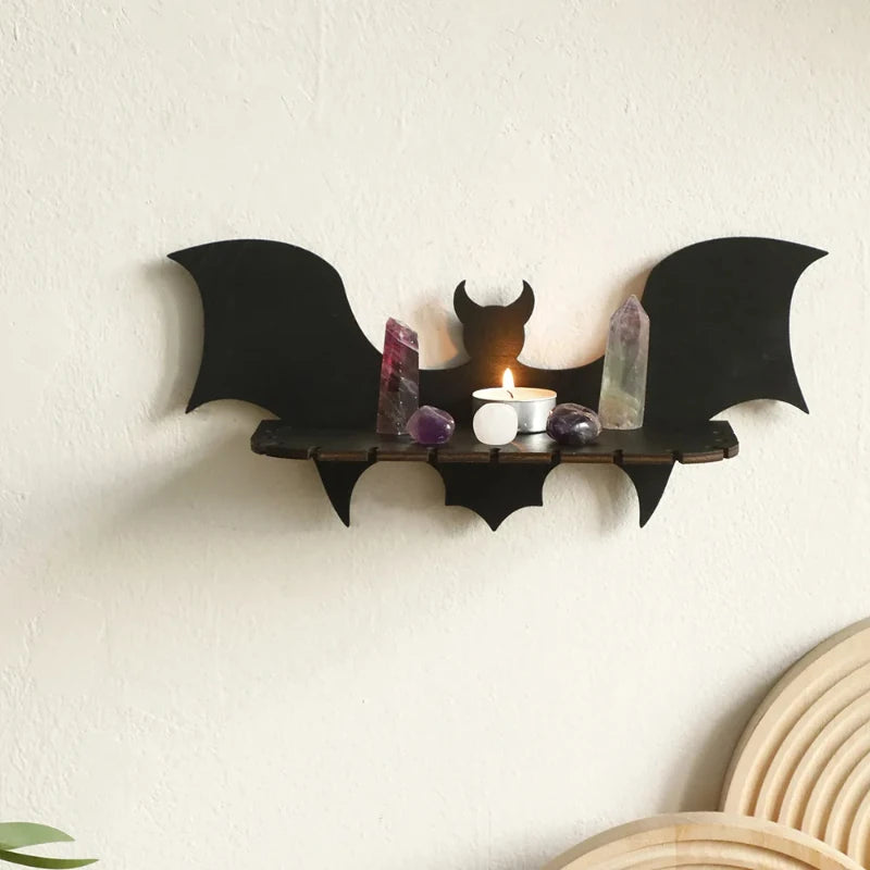 Bat-shaped wall shelf with a candle and crystals on a white wall.