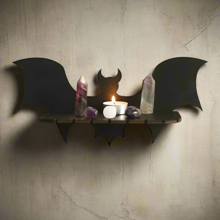 Bat-shaped wall shelf with a candle and crystals on a white wall.