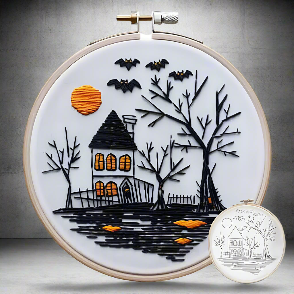 Embroidery hoop with Halloween-themed design of a haunted house, trees, and bats on a white background.