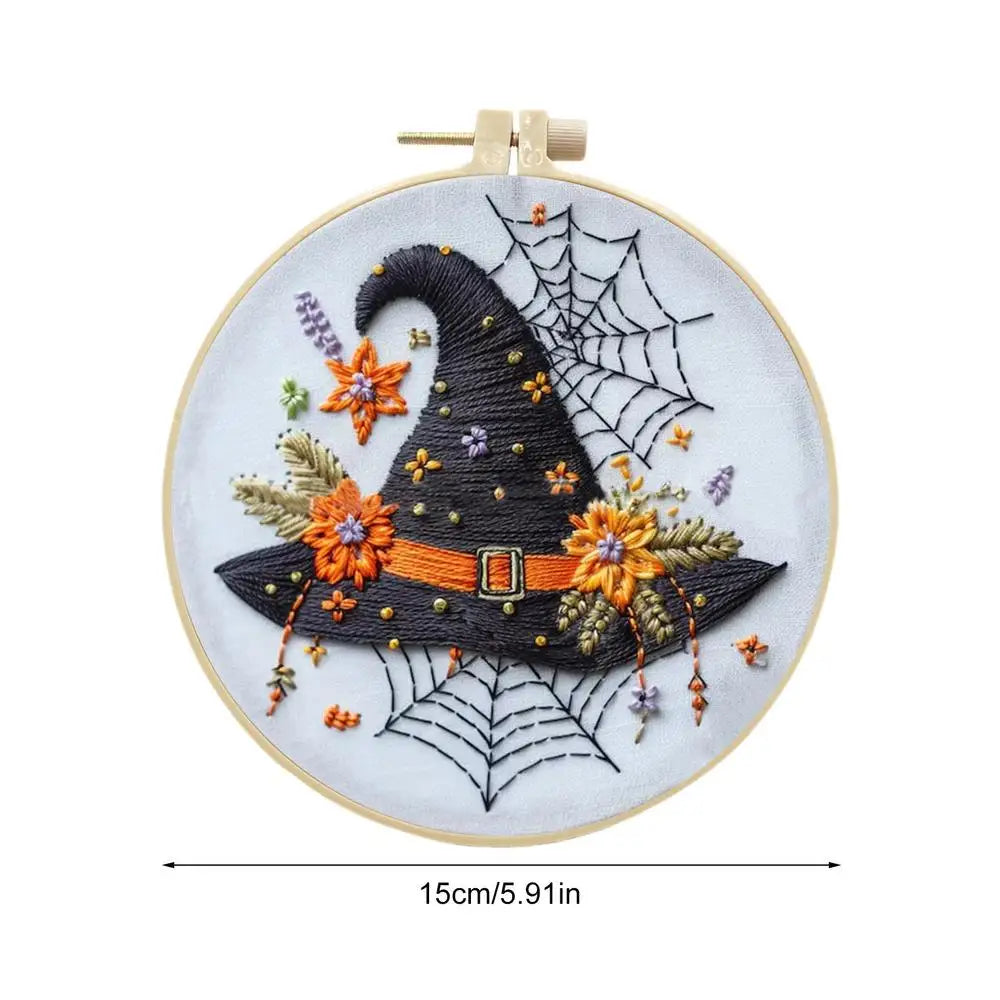 Embroidery hoop with a Halloween-themed design featuring a witch's hat, flowers, and spider webs.