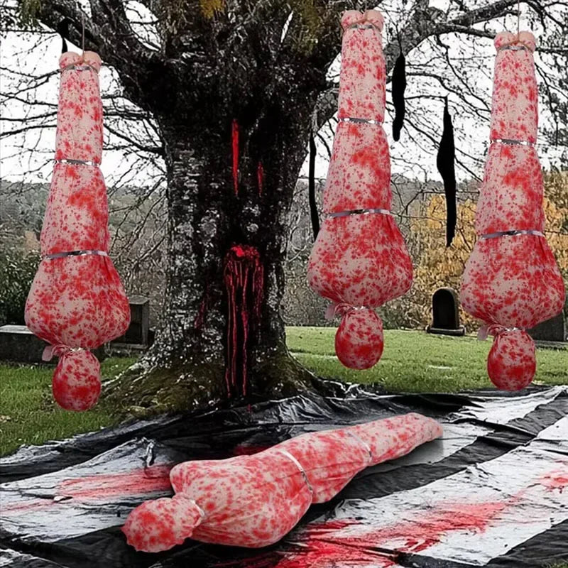 Red and white hanging objects resemblingorgans on a tree with a black tarp on the ground.