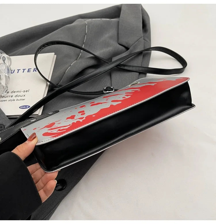 Black clutch with red and white design held by a hand, with a gray coat and magazine in the background.