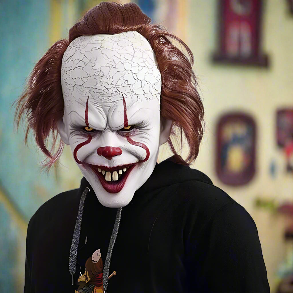 Person wearing a clown mask with red hair and a black hoodie on a white background