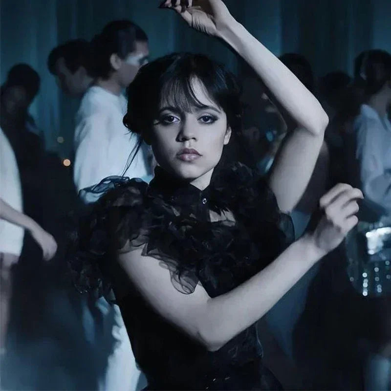 Woman in a black dress with sheer sleeves in a dimly lit room with other people.